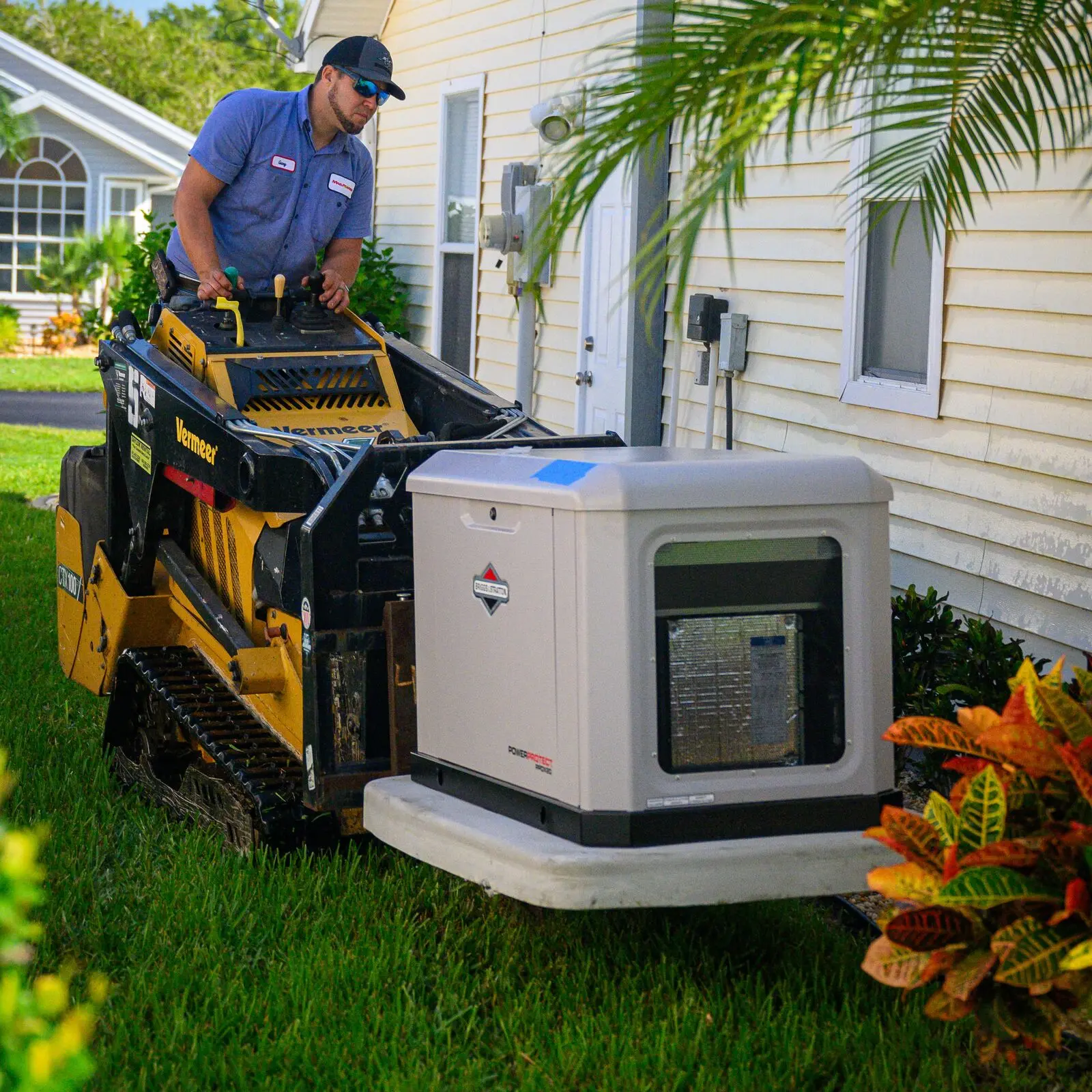 A technician placing a Briggs & Stratton standby generator on its pad with a compact track loader